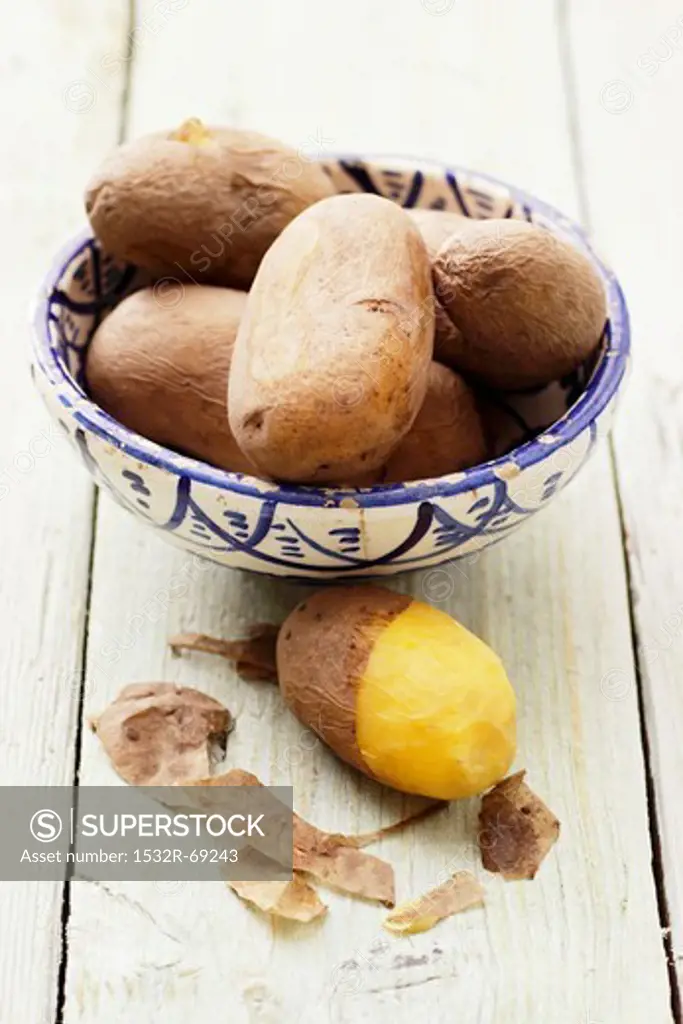 Potatoes cooked in their skins, in and next to a bowl