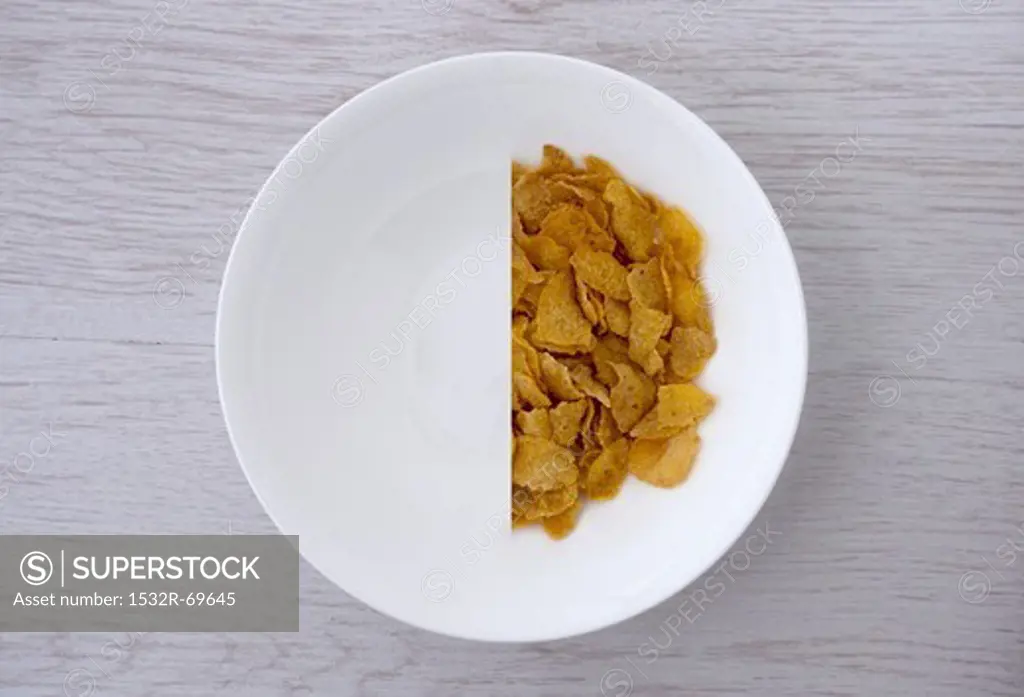 A halved portion of cornflakes in a white bowl (view from above)