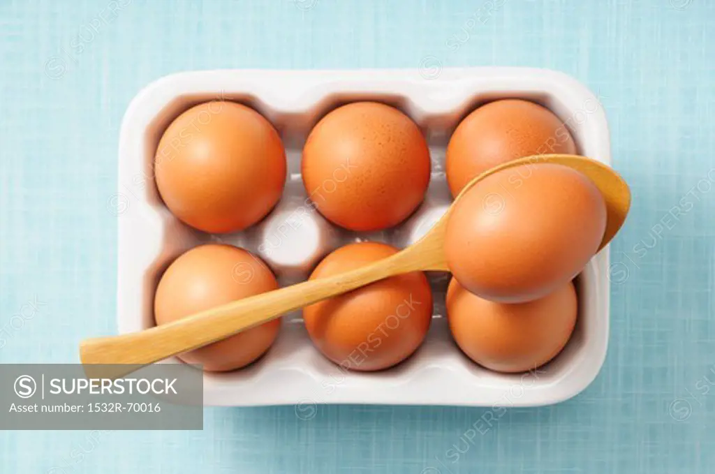 Brown eggs in a box and on a spoon (view from above)