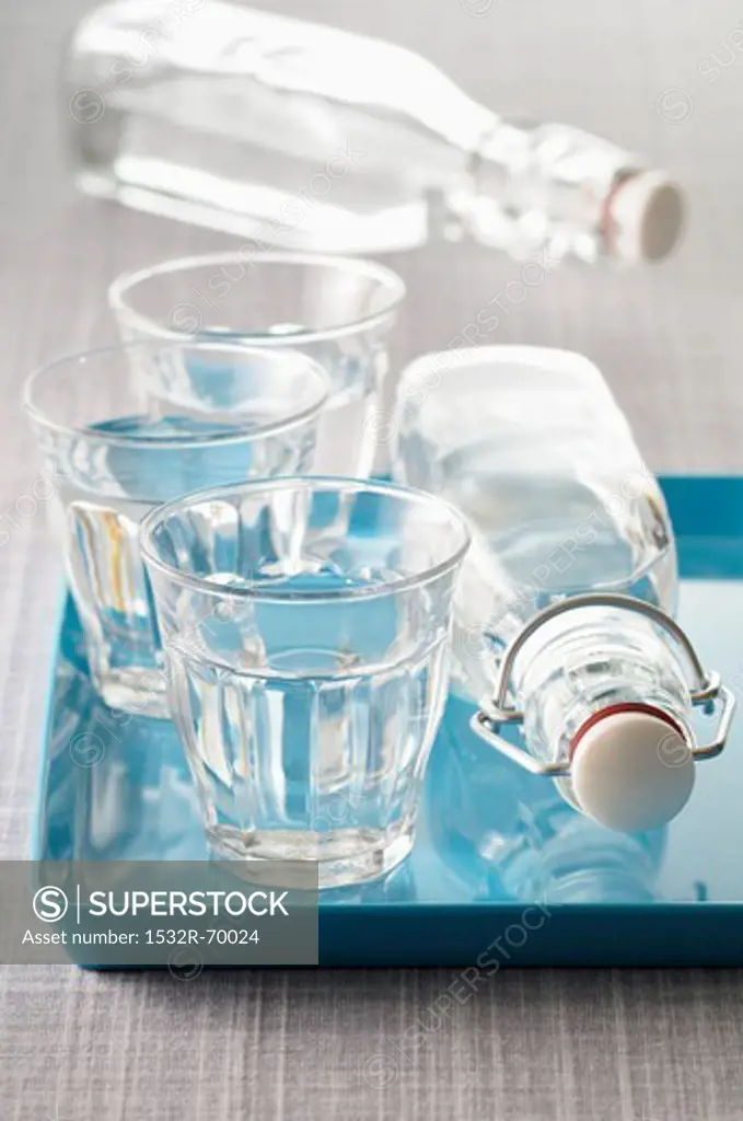 Three glasses of water and two bottles of water, some of these on a blue tray