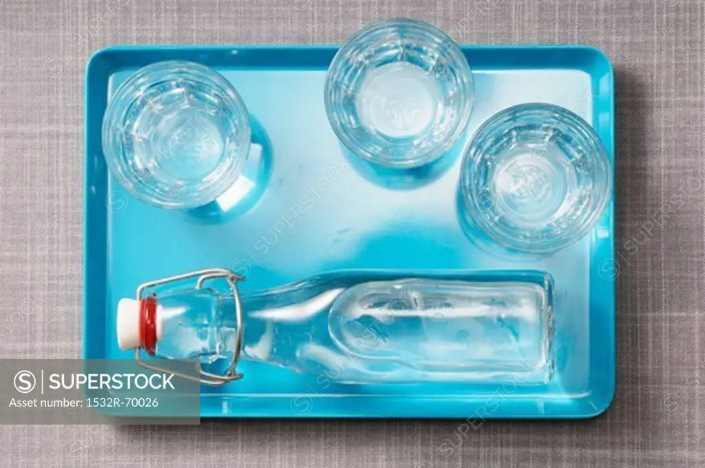 Three glasses of water and a bottle of water on a blue tray