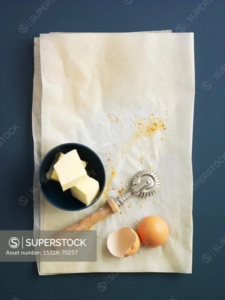 Butter, a pastry wheel and egg shells on grease-proof paper