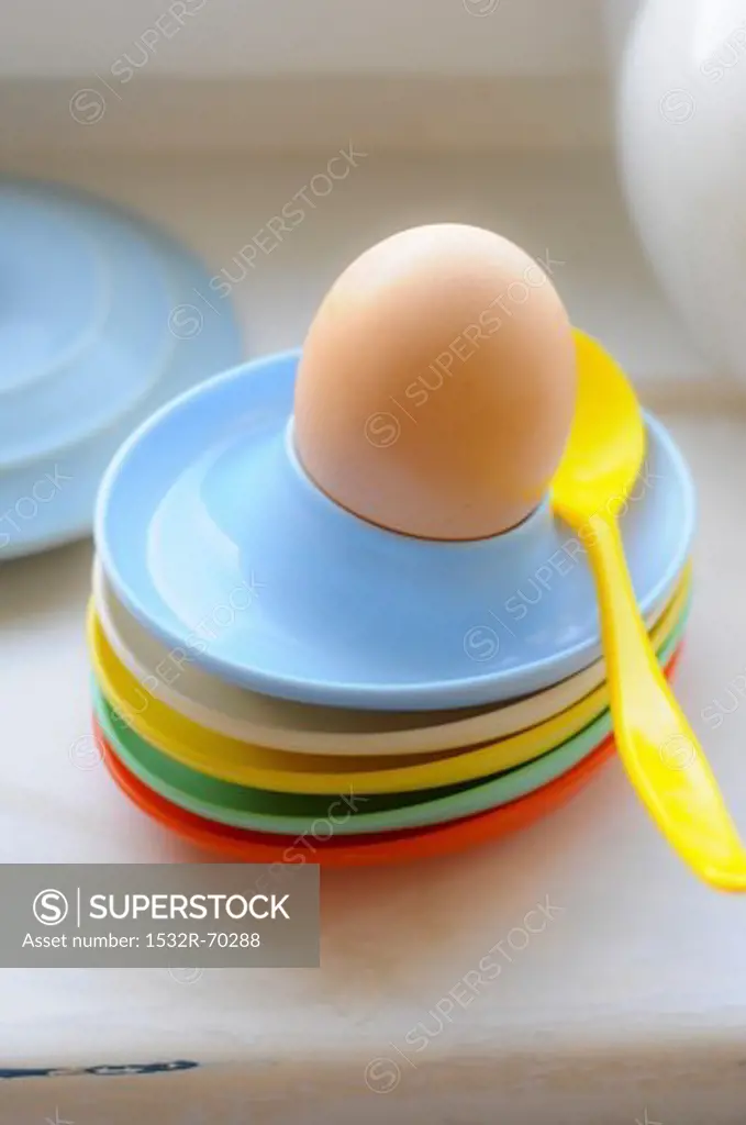 Colourful plastic egg cups and a boiled egg with a spoon
