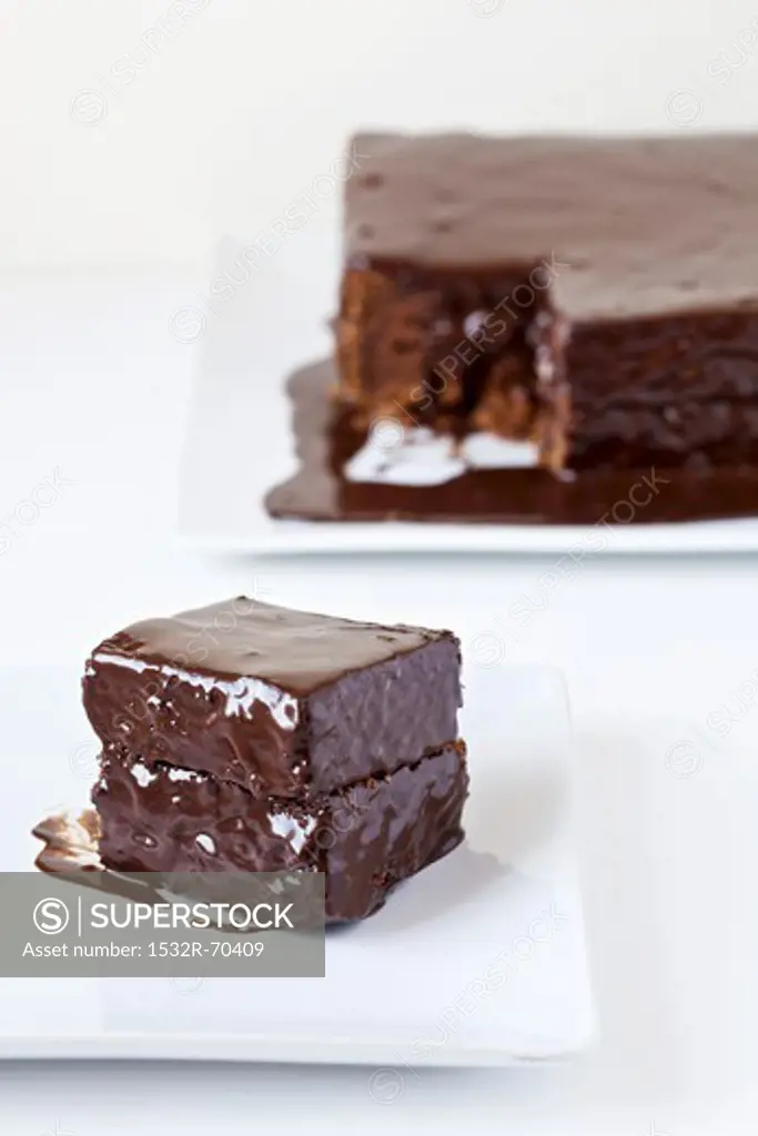 A Piece of Mud Cake on a White Plate; Remainder of Cake in the Background