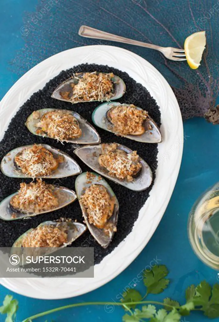 Green mussels topped with cheese and grilled, on a white plate with black salt