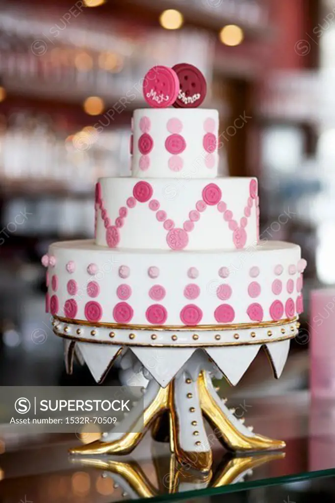 An unconventional wedding cake decorated with pink buttons on a gilded cake stand