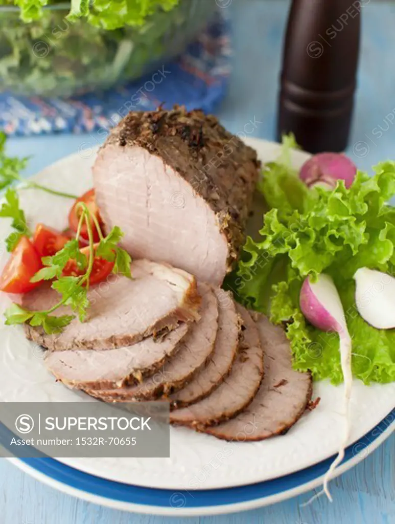 Partially Sliced Pork Roast on a Platter with Greens and Radishes