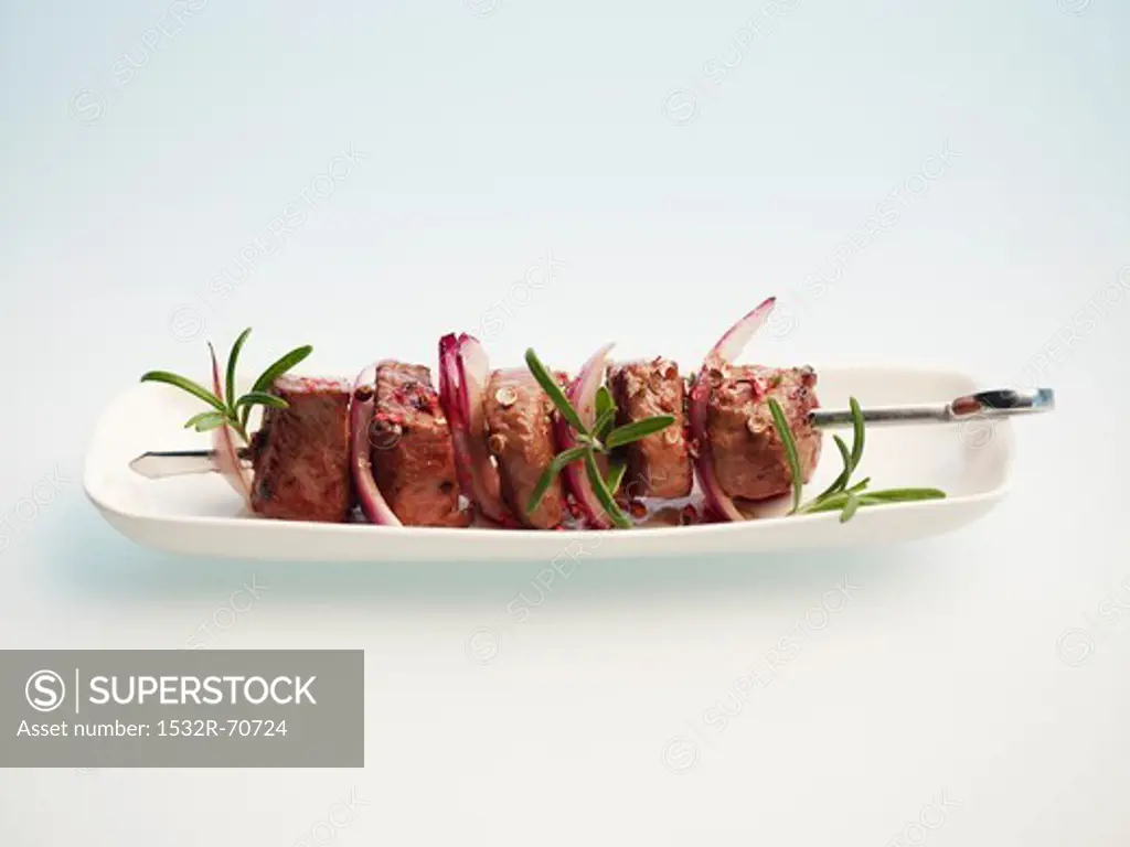 A lamb kebab on a plate against a white background