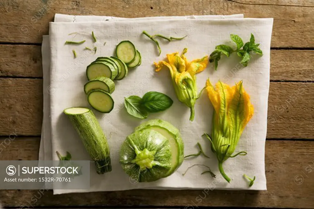 A still life featuring courgettes, courgette flowers and herbs