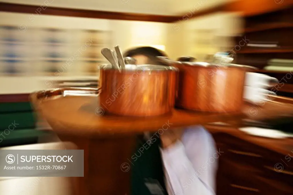 A waiter carrying a tray of copper pots