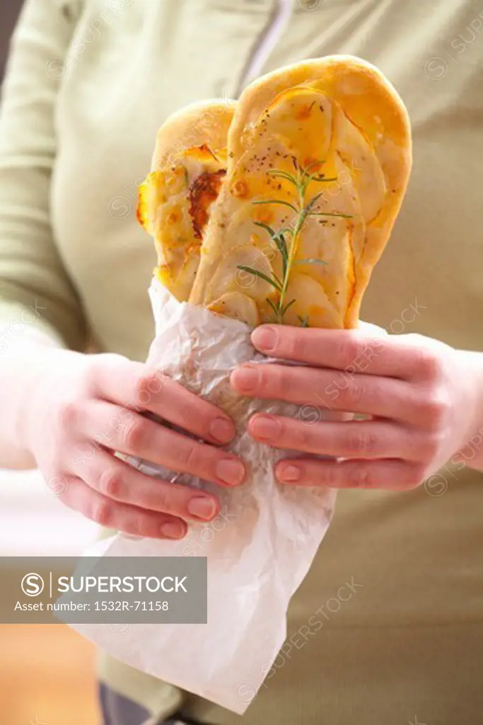 A woman holding snack-size oblong pizzas topped with potato and rosemary