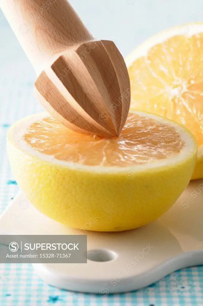 A halved grapefruit with a wooden lemon squeezer