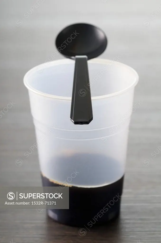 A plastic cup with a plastic spoon and the end of a cup of coffee