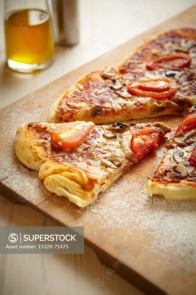 Pizza with salami, tomatoes and mushrooms on a wooden board