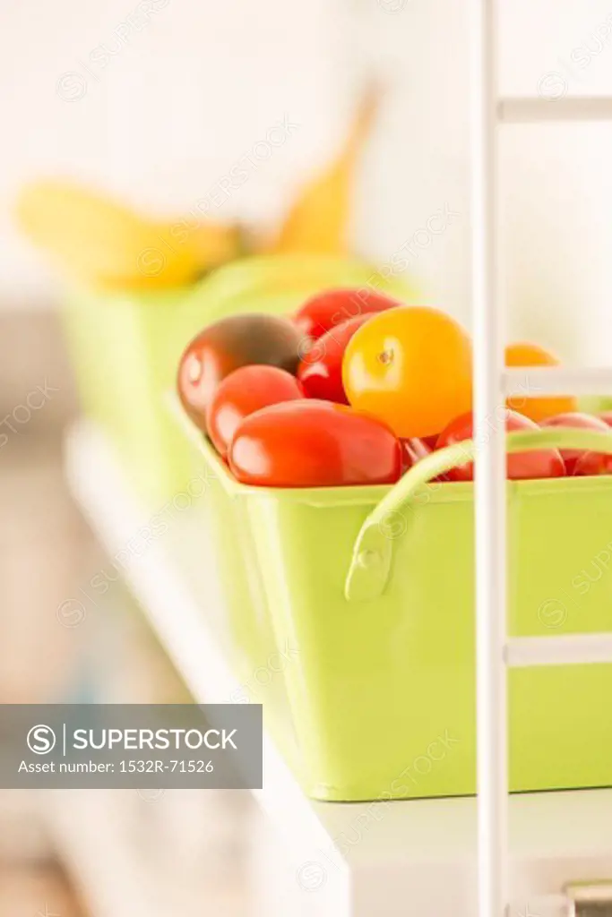 A green metal box full of assorted tomatoes on the kitchen shelf