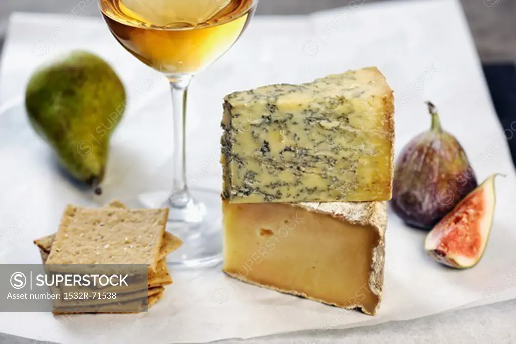 Assorted types of cheese with figs, a pear, crackers and a glass of white wine