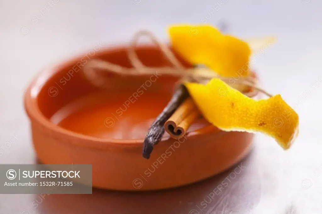 Lemon peel, a cinnamon stick and a vanilla pod on a ramekin