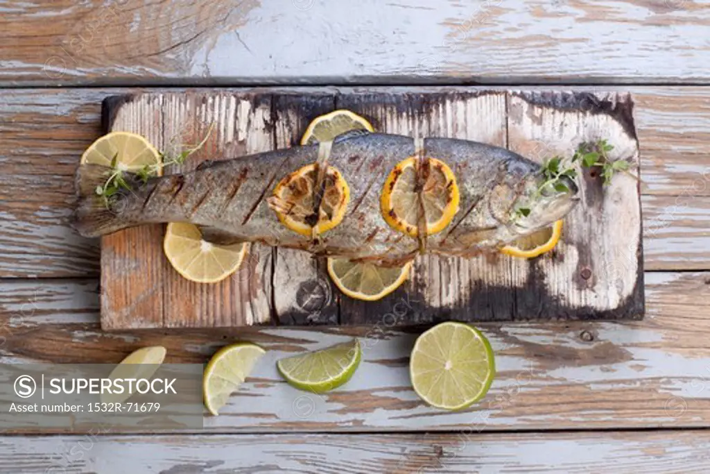 Barbecued trout with lemons and limes on a wooden board