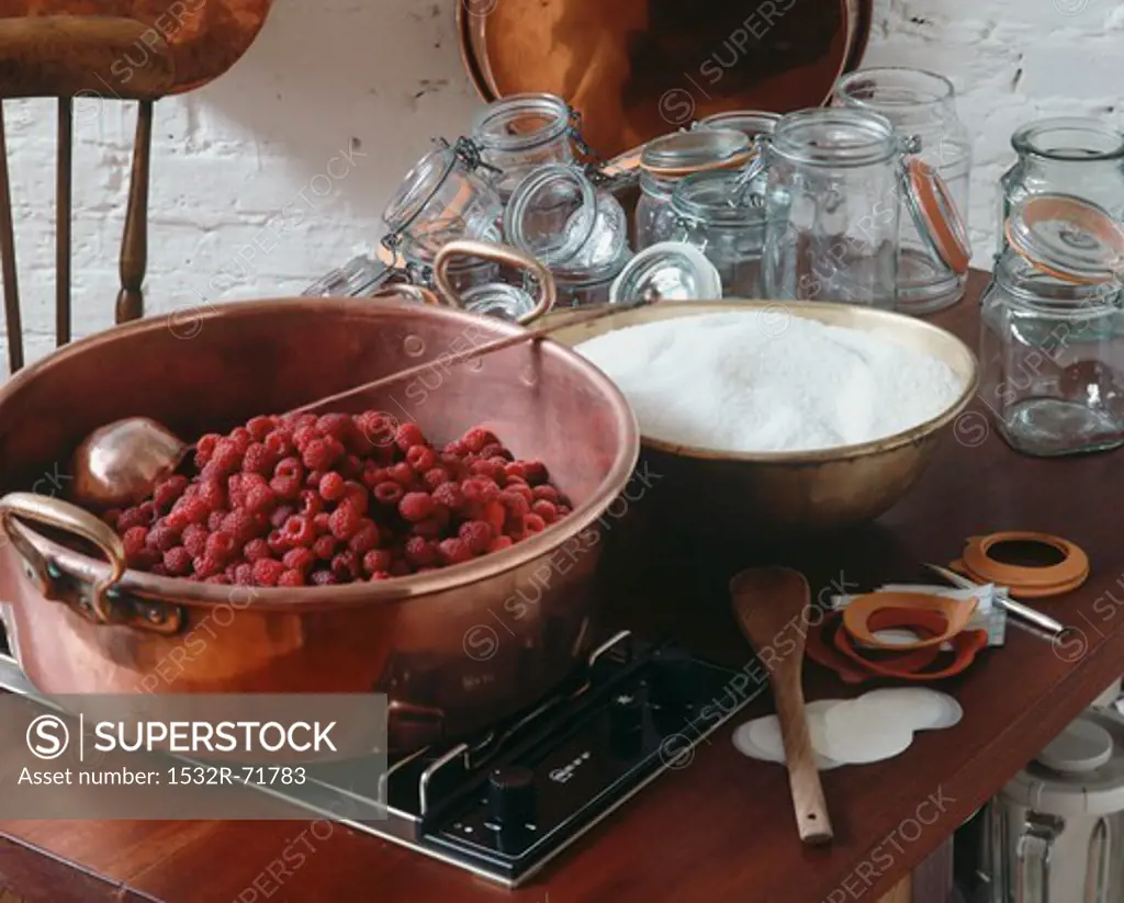 Copper pans (raspberries and sugar) on gas rings, glass jars behind.