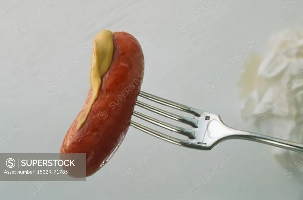 Sausage cooked on a fork with mustard half way along it.