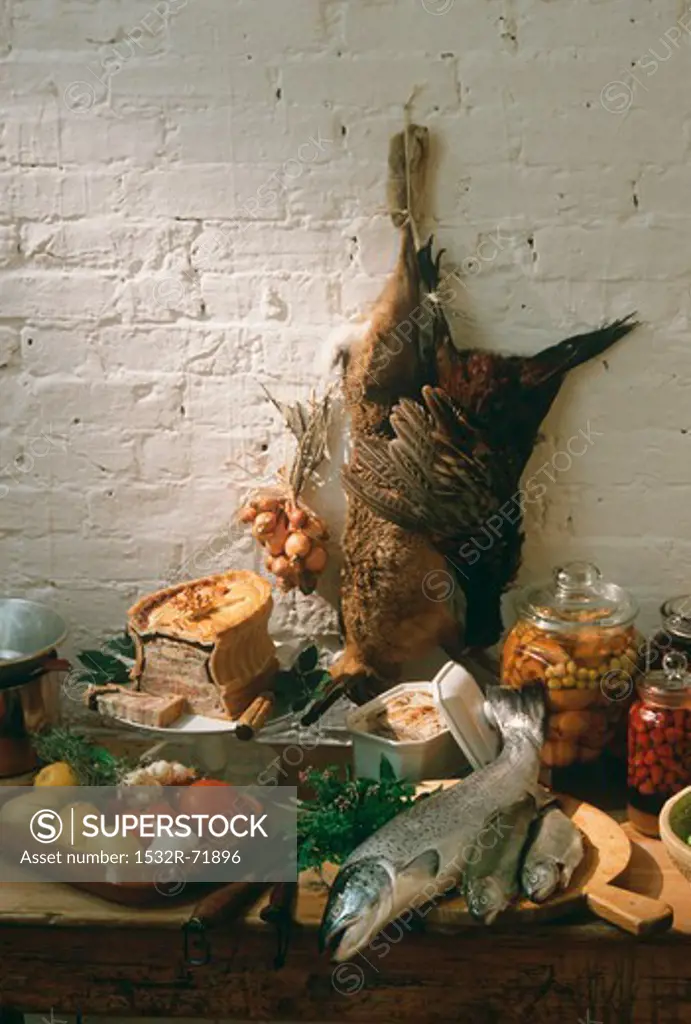 An autumnal still life featuring game, terrines, fish, vegetables and bottled fruit