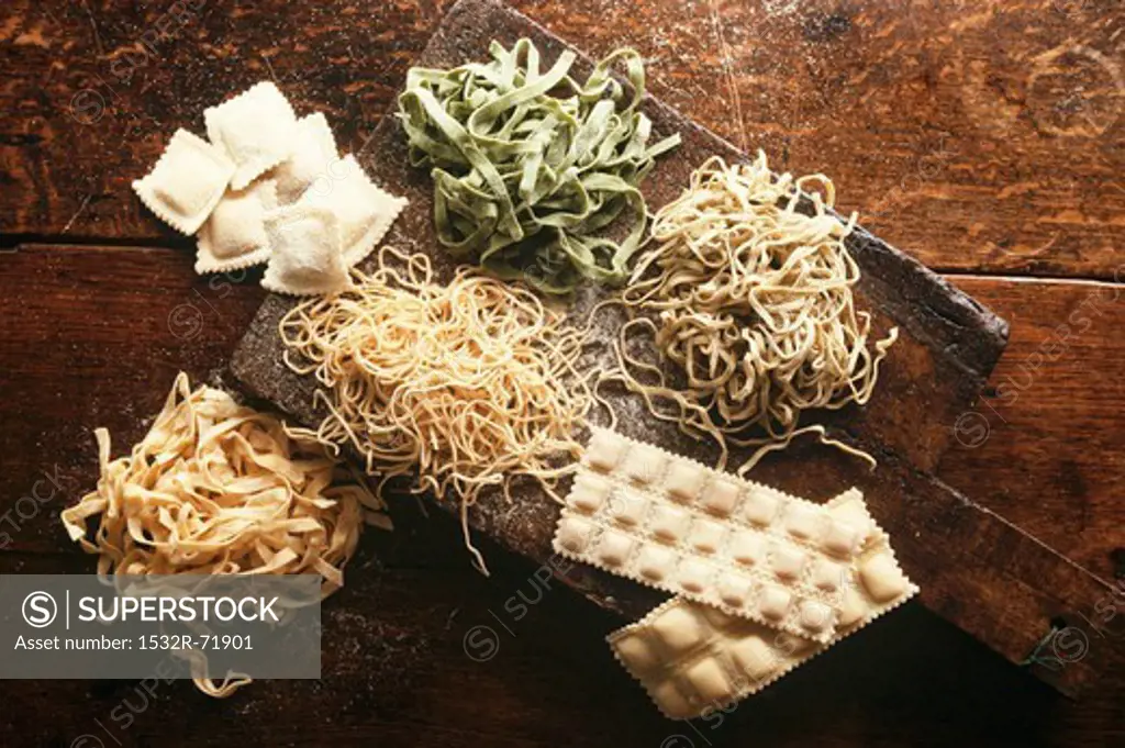 Pasta - raw pasta on old wooden board, wood background, ravioli, green tagliatelle, ravioli in sheets