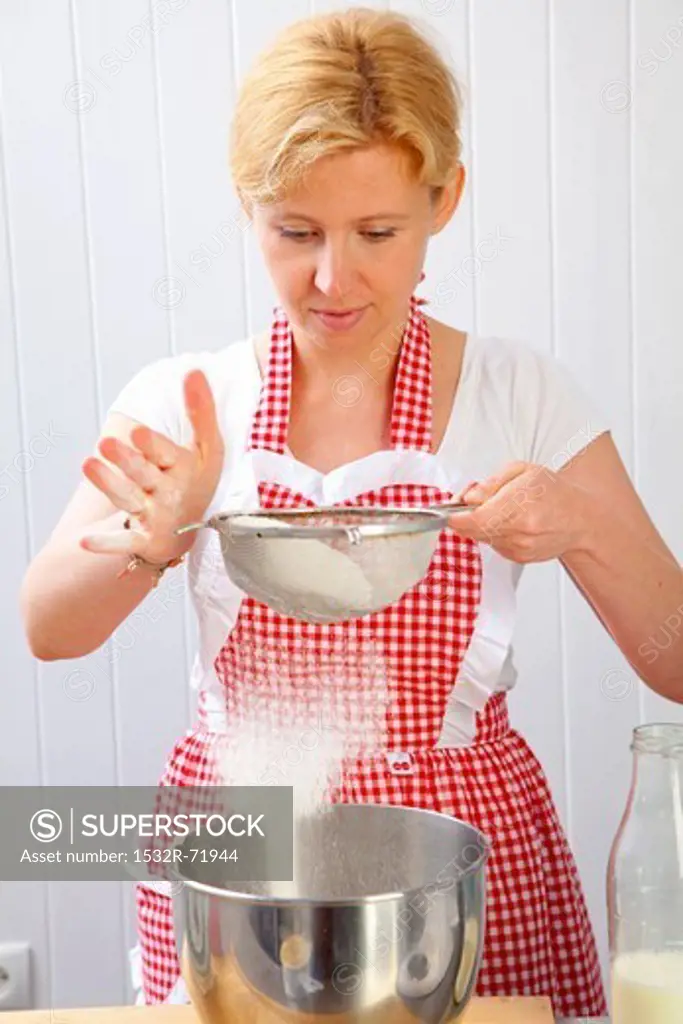 A woman sieving flour into a mixing bowl