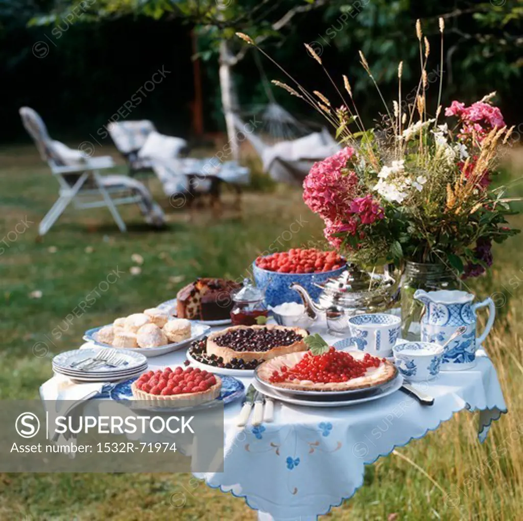 Summer afternoon tea setting - raspberry tart, blackcurrant tart, scones, fruit cake, red currant and apple tart.