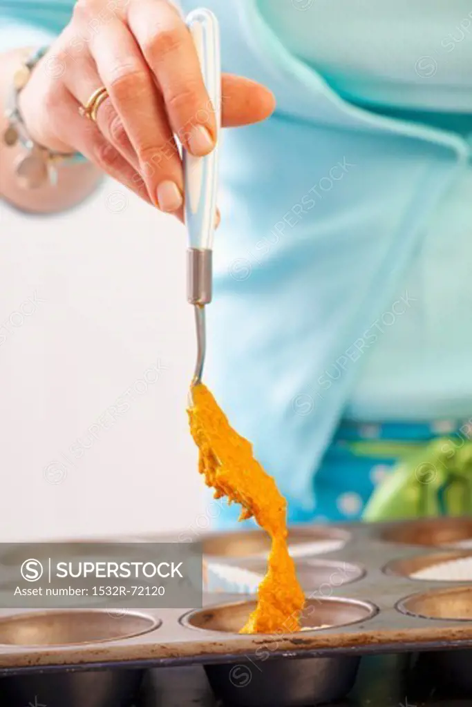 A woman spooning carrot cake batter into a baking tin