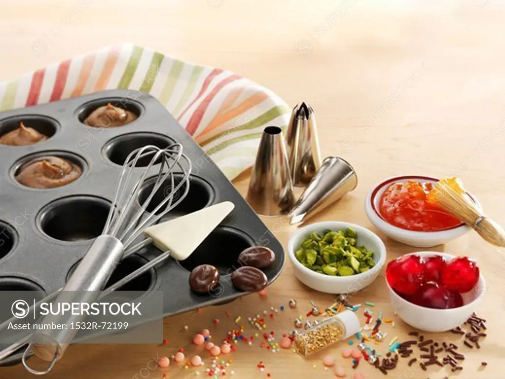 A muffin tray with batter, baking utensils and toppings