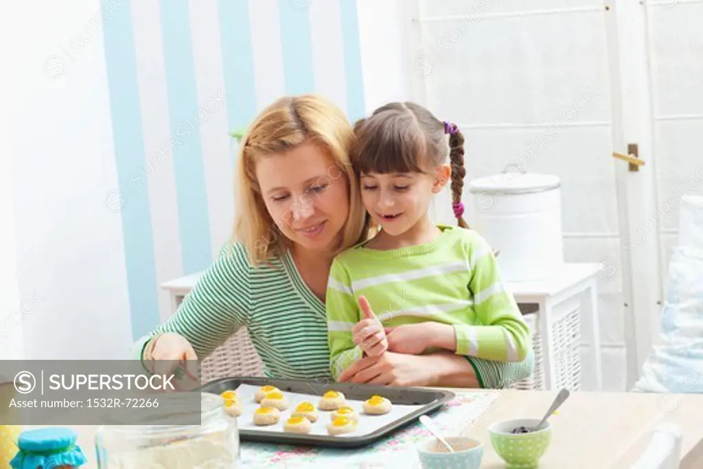A mother and daughter with a baking tray with unbaked jam biscuits