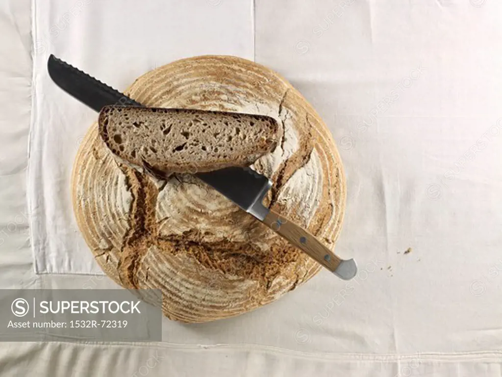A brown loaf, with a bread knife and a slice of bread lying on top of it
