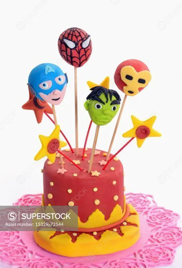 Cake pops decorated to look like superheroes, stuck into a cake