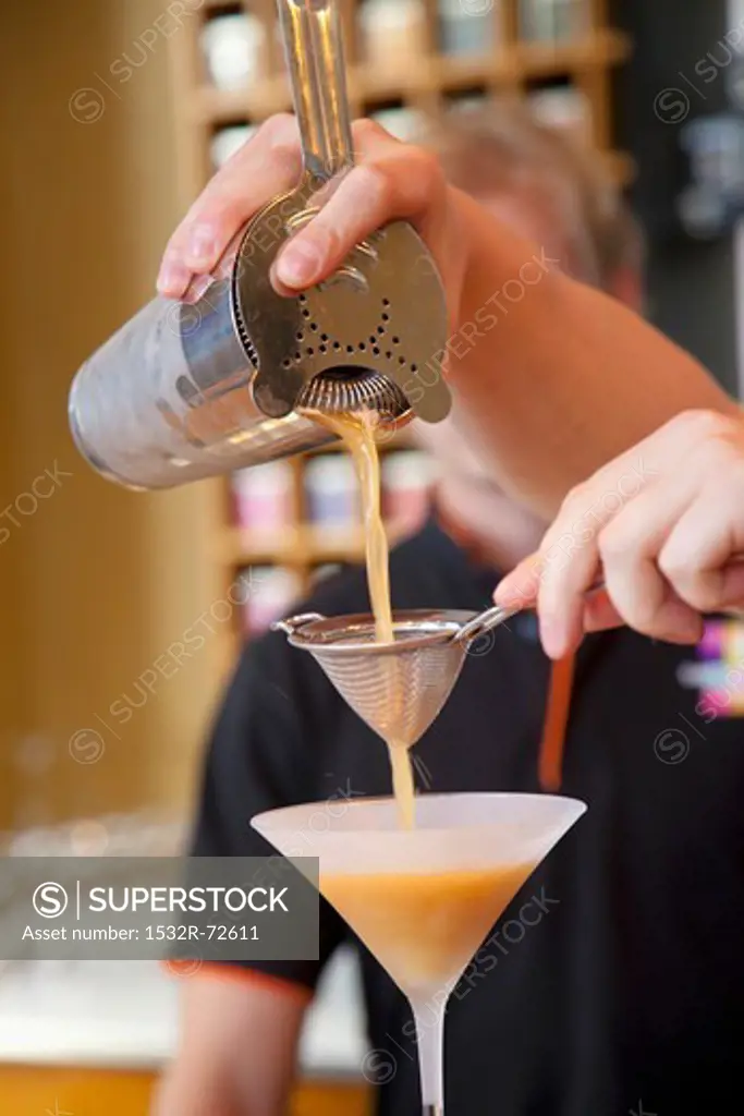A man pouring iced tea from a shaker into a cocktail glass