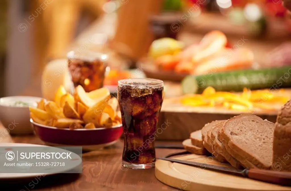 A table set with bread, potato wedges, raw vegetables and cola