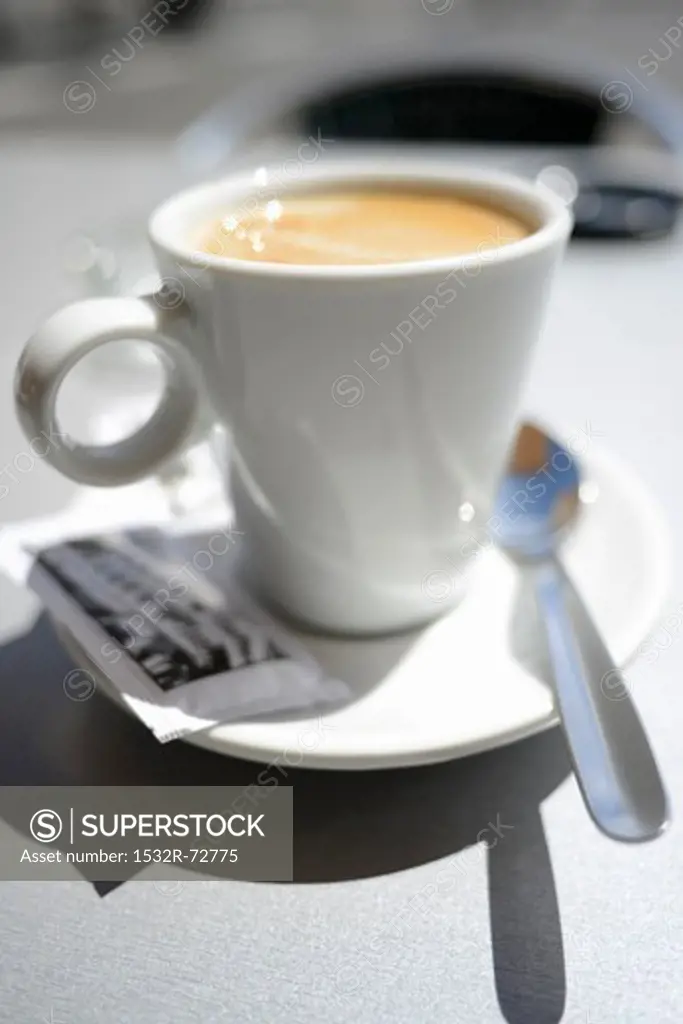Latte in a white cup with a packet of sugar and a spoon