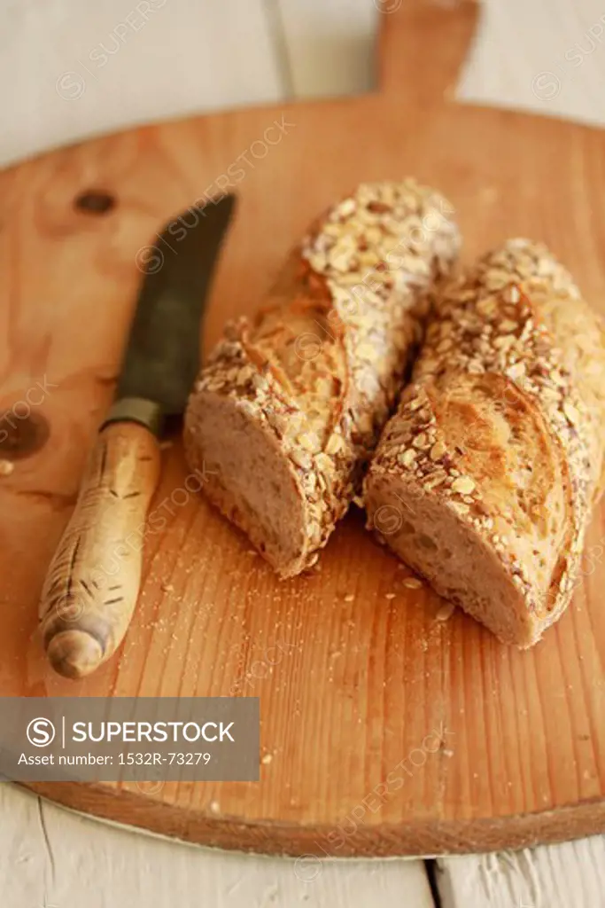 Halved wholegrain baguette with a knife on a wooden board, 8/9/2013