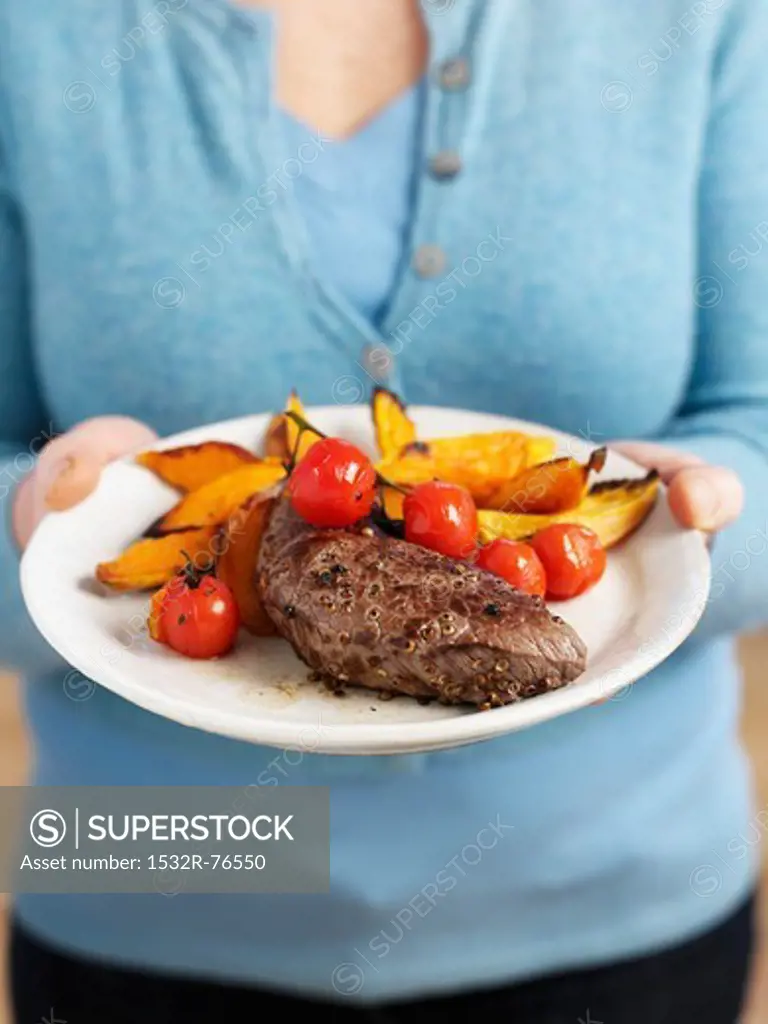 A woman holding a plate of beef steak, tomatoes and sweet potato chips, 11/14/2013