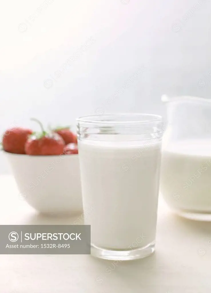 Glass of milk and milk jug; strawberries in white bowl