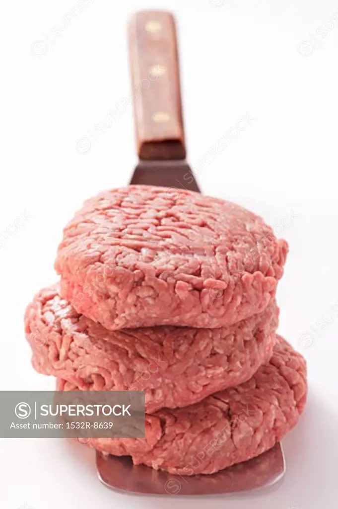 Three raw burgers in a pile on spatula