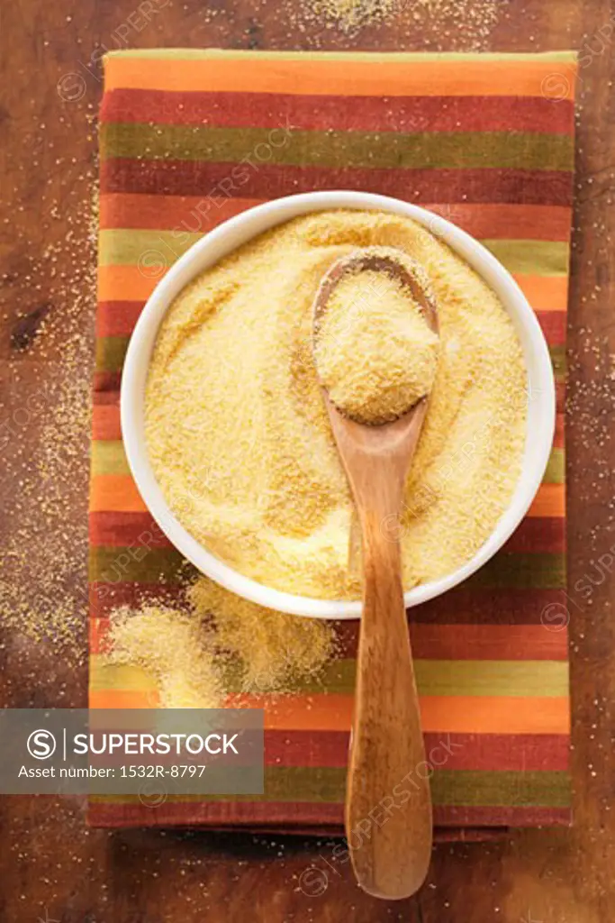 Polenta in bowl with wooden spoon on coloured cloth