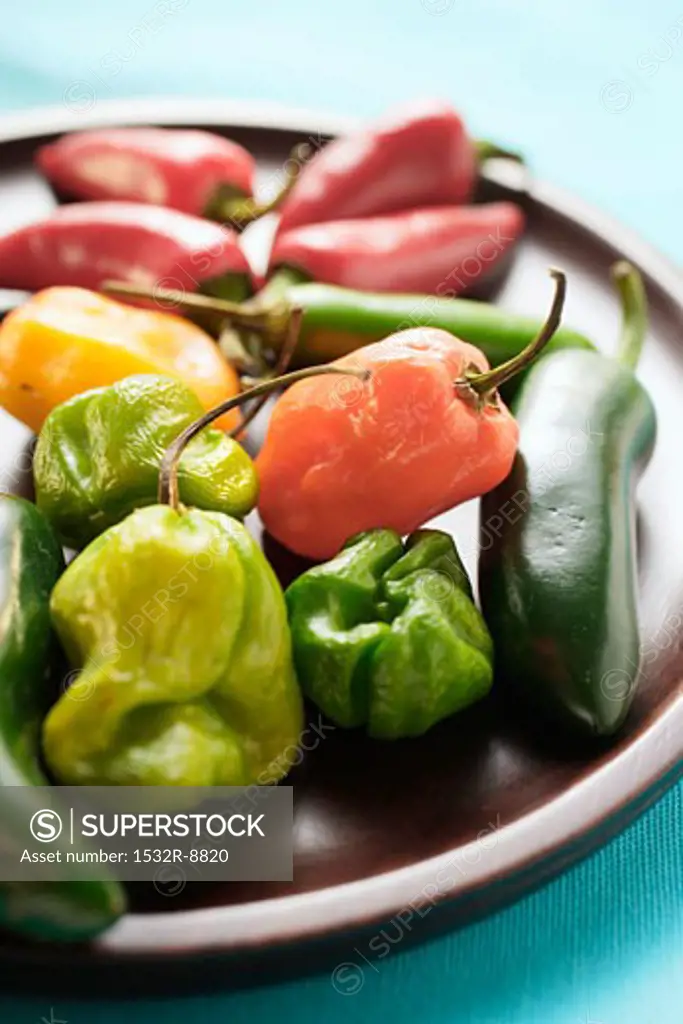Various chili peppers on wooden plate