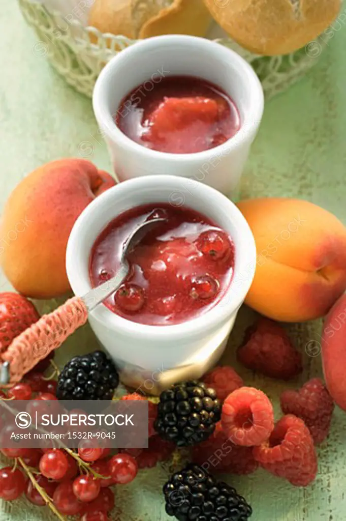 Mixed-fruit jam in small bowl, surrounded by fresh fruit