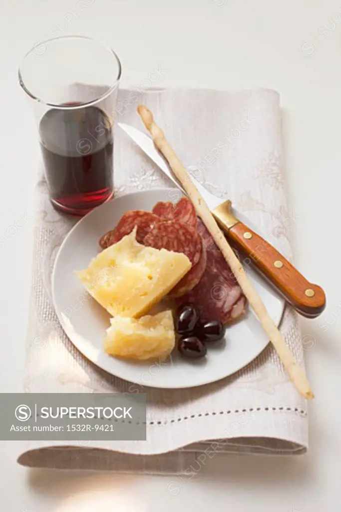 Salami, cheese, olives & grissini on plate, glass of red wine
