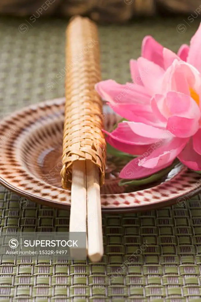 Chopsticks in woven wrapper with water lily on plate