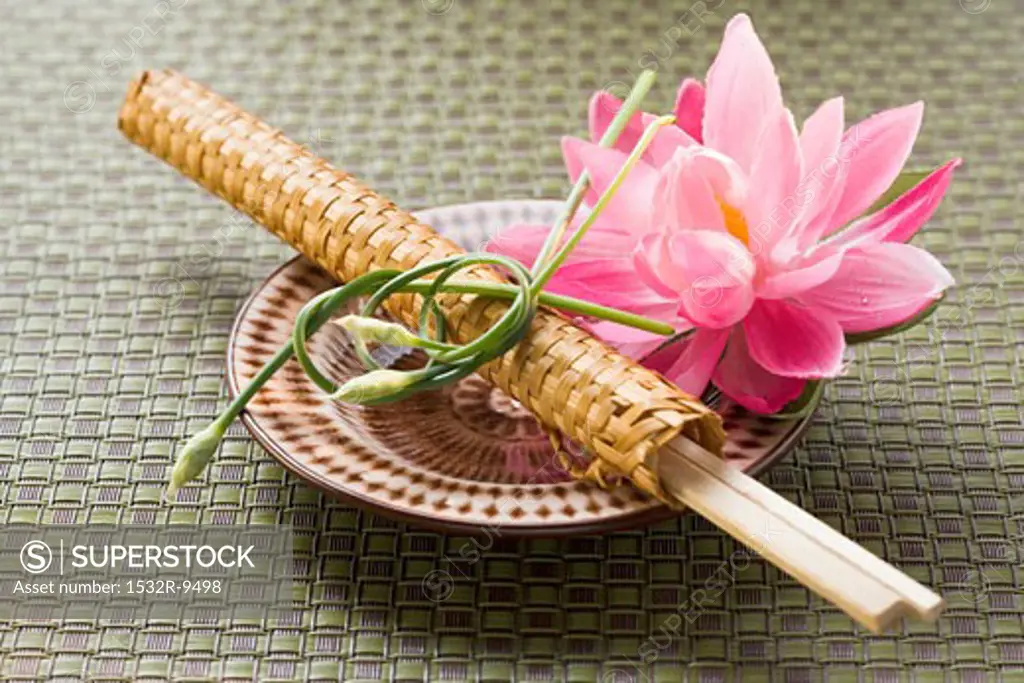 Chopsticks in woven wrapper with water lily on plate