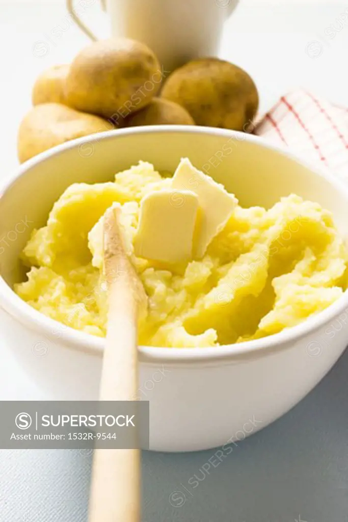 Mashed potato with butter in bowl with wooden spoon