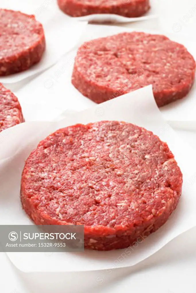 Several raw burgers on paper