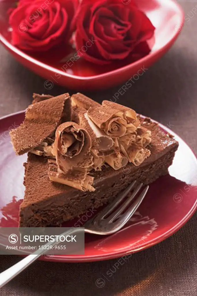 Piece of chocolate cake with chocolate curls, red roses