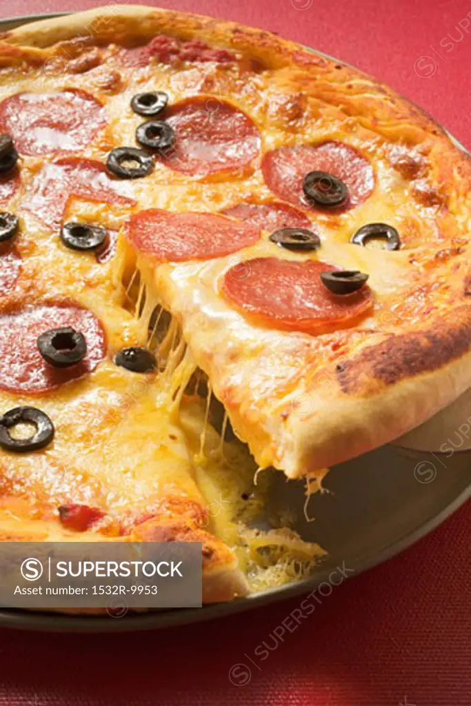 Pizza with salami, cheese and olives, a piece cut